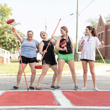 Load image into Gallery viewer, Off-guard photo of four women holding paint rollers and brushes  standing behind the edge of painted crosswalk
