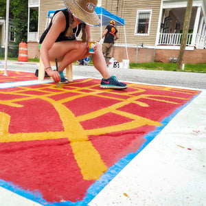 Mama Hawk painting crosswalk mural with orange and red paint