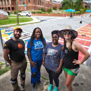 One man and three woman smile for a picture in front of the completed crosswalk with view of horizontal and vertical crosswalk designs