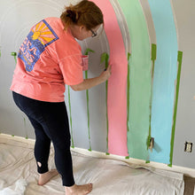 Load image into Gallery viewer, Abby works on adding a second coat to the warm pink strip in E&#39;s rainbow mural. 
