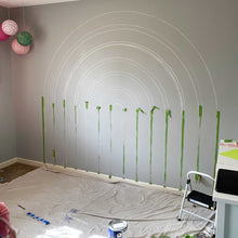 Load image into Gallery viewer, The beginning of E&#39;s rainbow mural. A dark gray wall with the rainbow stripes chalked out and painter&#39;s tape in place to begin painting.
