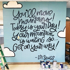 Blue painted mural with text "you'll move mountains! today is your day! your mountain is waiting so... get on your way! -dr. seuss" with clouds and black lettering
