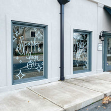 Load image into Gallery viewer, Close-up of two glass windows separated by a pole on a building. The windows have green diamond shapes and dots; the left window has &quot;Sparks Yoga&quot; painted in white, and the right window has &quot;what sparks your soul?&quot; painted in white paint.
