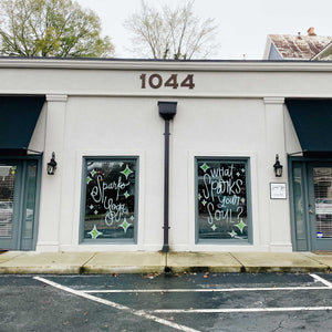 Two glass windows separated by a pole on a building. The windows have green diamond shapes and dots; the left window has "Sparks Yoga" painted in white, and the right window has "what sparks your soul?" painted in white paint.