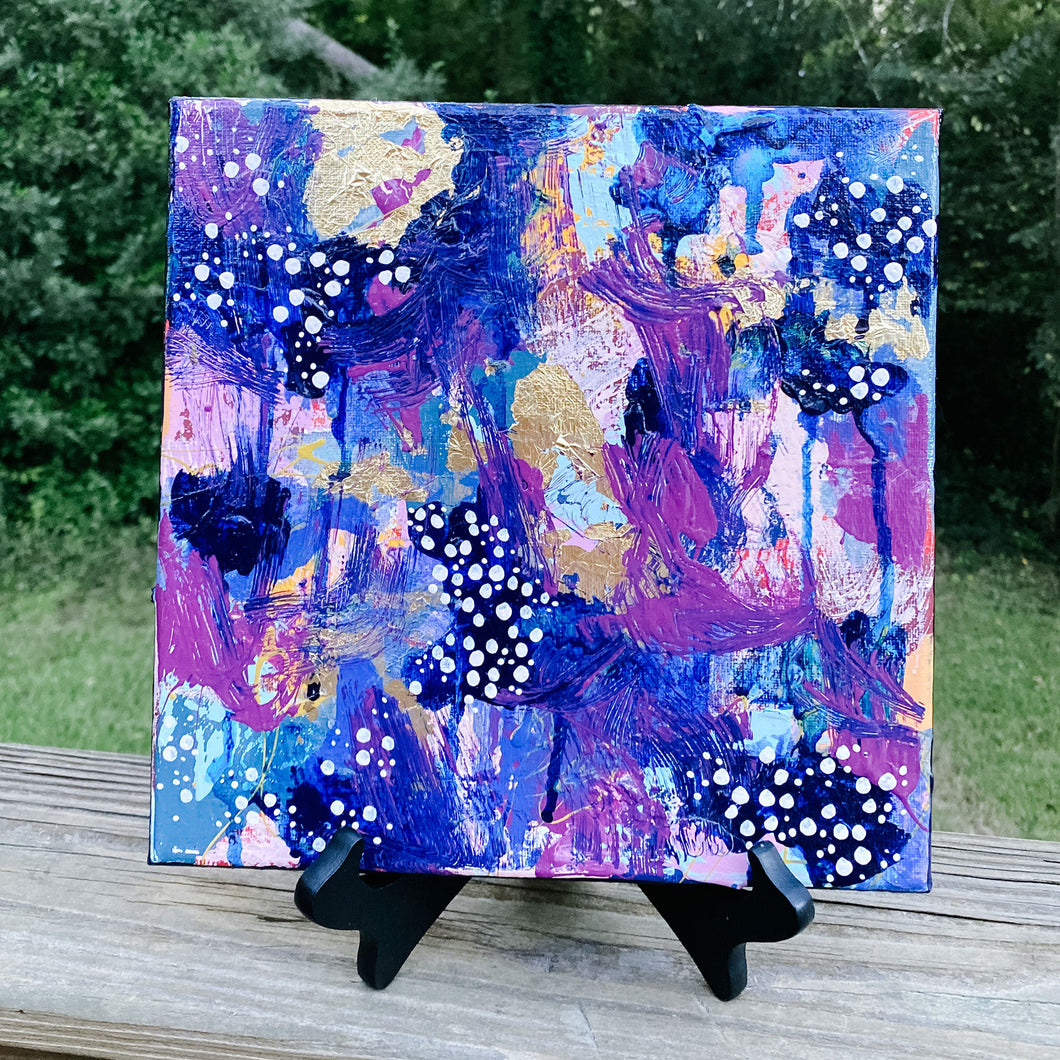 Multicolored abstract painting on canvas on wooden railing with greenery in the background