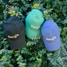 Load image into Gallery viewer, Three hats, black, green, and blue with &quot;georgia&quot; text with an orange peach as the &quot;o&quot; and greenery in the background
