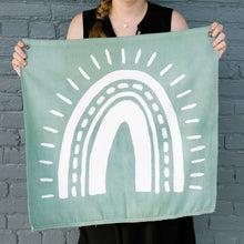 Load image into Gallery viewer, Erin from Mama Hawk Draws holds a 2&#39;x2&#39; green colored drop cloth with a white rainbow painted on it. The rainbow&#39;s four stripes have different thicknesses with one stripe made of dashes. Outside the stripes are rays around the rainbow.
