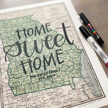 Load image into Gallery viewer, Close up of Vertical vintage style map of Georgia with hand-lettered text that says &quot;Home sweet home&quot; with two pens laying on the right side
