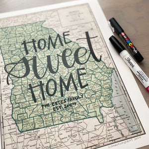 Close up of Vertical vintage style map of Georgia with hand-lettered text that says "Home sweet home" with two pens laying on the right side