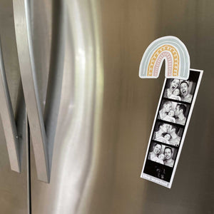 Pink, yellow, and blue rainbow magnet holding up family photos on a fridge