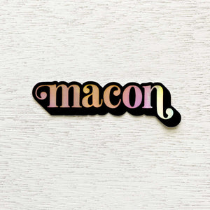 Black bordered, holographic "macon" sticker on white wooden background.
