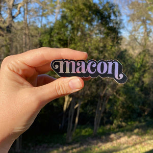 Woman's hand holding black and holographic with "macon" text.