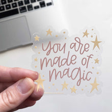 Load image into Gallery viewer, Woman holds a clear sticker with yellow stars on the border and pink hand lettering that reads &quot;you are made of magic.&quot; The sticker is being held with a computer in the background.
