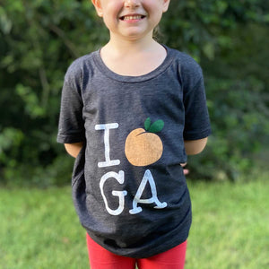 Young child smiling wearing the "i heart GA" tee with grass and trees in the background