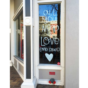 Sidewalk view of a slender glass window with "all you need is love (and shoes)" painted in white