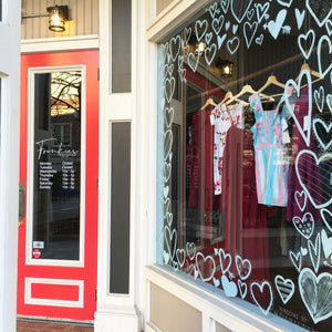 Sidewalk view of Frankie's boutique of window painted with different shaped and patterned hearts in white paint.